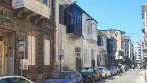 A cobblestone street lined with historic buildings, parked cars, and a clear blue sky. - Historical House in Alsancak (Izmir)