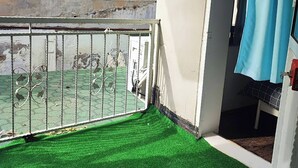 A balcony with a metal railing, a green artificial turf floor, and a partially visible wall with peeling paint. - Historical House in Alsancak (Izmir)