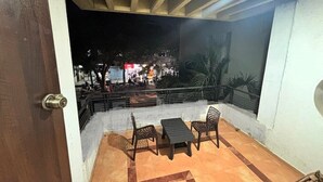 Un balcone con tavolo e sedie, vista su una strada animata di sera, e una porta che conduce all'interno.