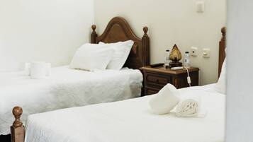 A hotel room with two wooden beds, white linens, a bedside table with a lamp, and a power outlet.