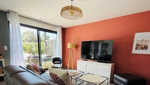 Een moderne woonkamer met een bank, een televisie, een lamp en een schuifpui die uitkomt op een buitengebied.