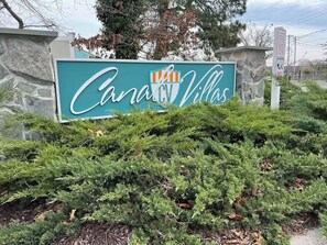 Schild für 'Canal RV Villas' mit einer Steinmauer und dichtem Buschwerk im Vordergrund.