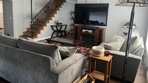 A living room with a sofa, a coffee table, a TV, a lamp, and a staircase. - Century Farm in Horse Heaven Hills, Tri-Cities WA (Kennewick)