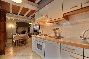Une cuisine avec des poutres en bois, des meubles blancs, une cuisinière et un évier.