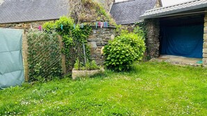 A stone building with a grassy yard, a clothesline with clothes, and a covered area. - Gîte 4 persons Plestin-les-Grèves (Plestin-les-Grèves)
