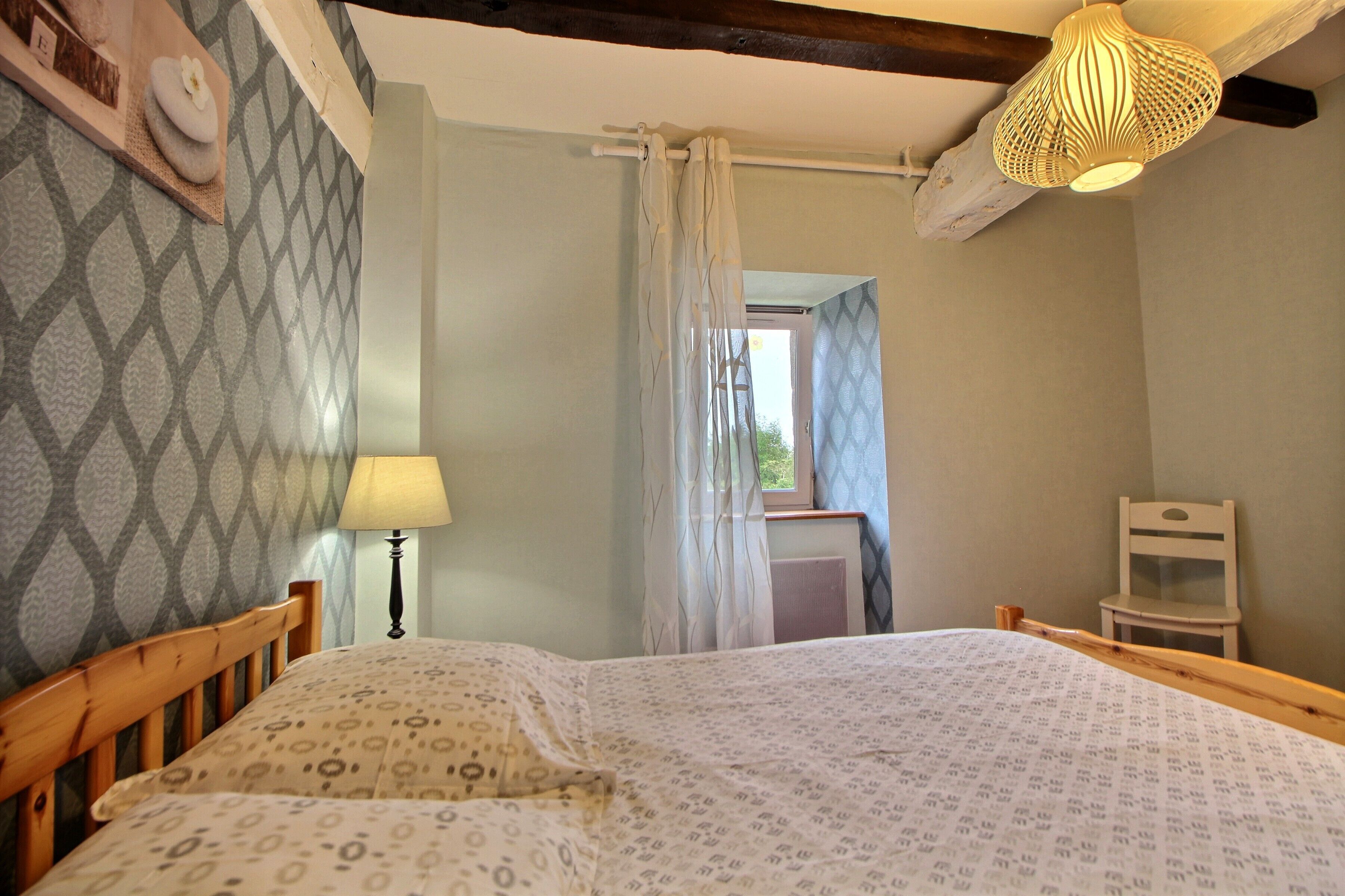 Een slaapkamer met een bed, een bedlampje, een stoel en een raam met gordijnen.