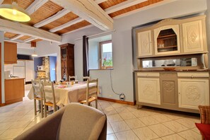 Une cuisine spacieuse avec des poutres en bois, un coin repas avec une table et des chaises, et une vue par la fenêtre.