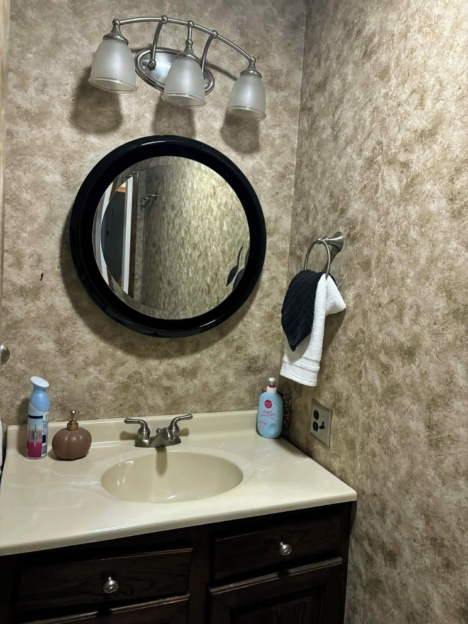 A bathroom with a round mirror, a sink, a towel rack, and a light fixture.