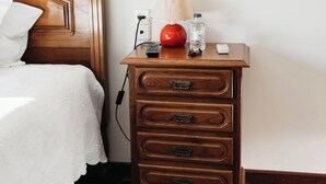 Un letto rifatto con cura, una testiera e un comodino in legno con cassetti, una lampada, una bottiglia d'acqua e un telecomando.