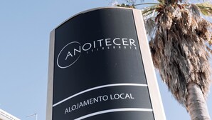 A sign for 'ANOITECER ALOJAMENTO LOCAL' with a palm tree in the background.