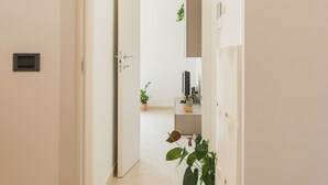 En hall med en dörr som leder in till ett rum, en krukväxt och ett litet bord med diverse föremål på.