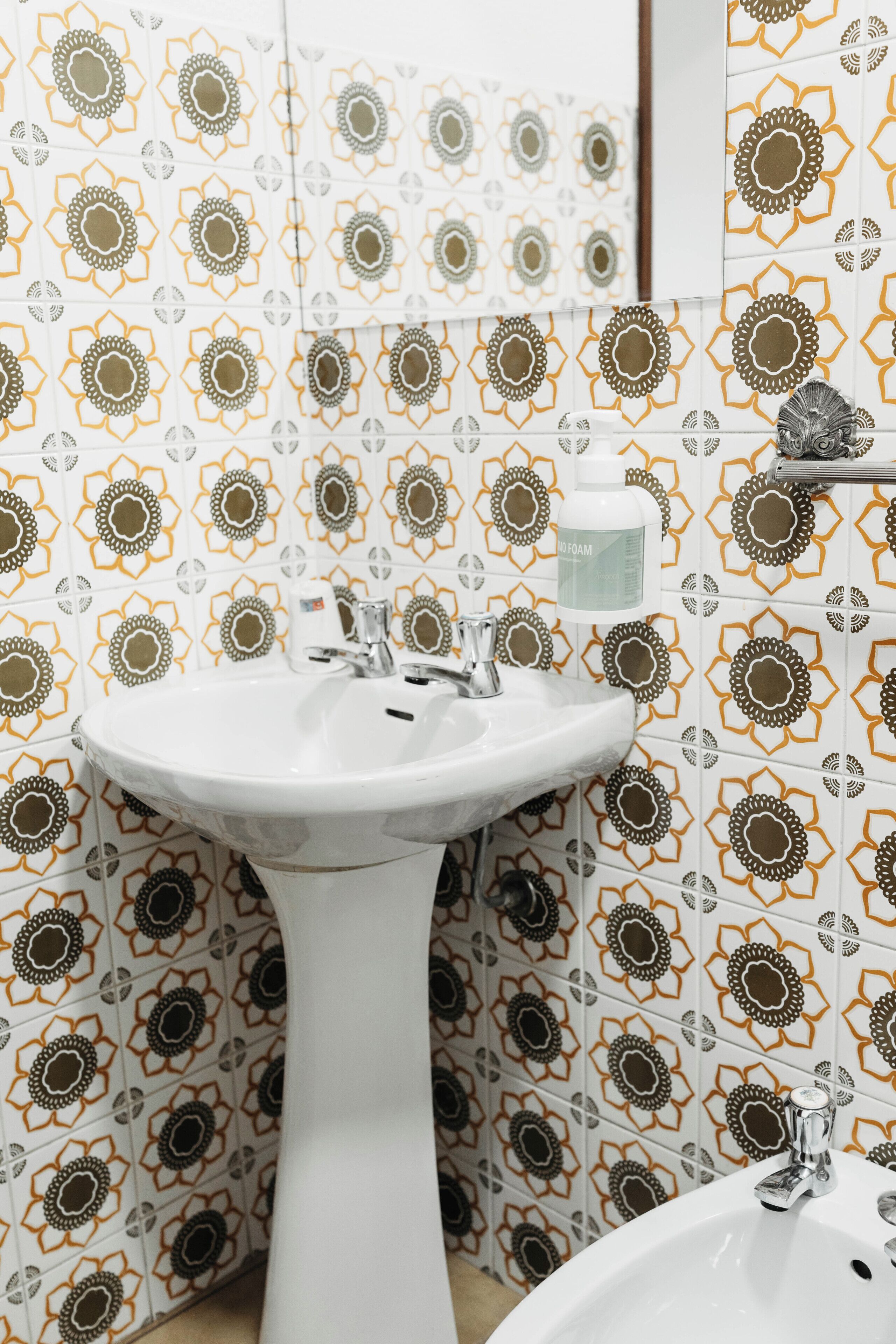 Un baño con lavamanos pedestal, un espejo y azulejos estampados.