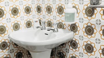 Un baño con lavamanos pedestal, un espejo y azulejos estampados.