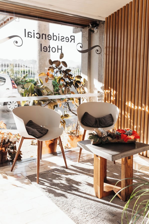 A hotel reception area with two white armchairs, a small wooden table with a decorative arrangement, and a window with the text 'Hotel Residence'.