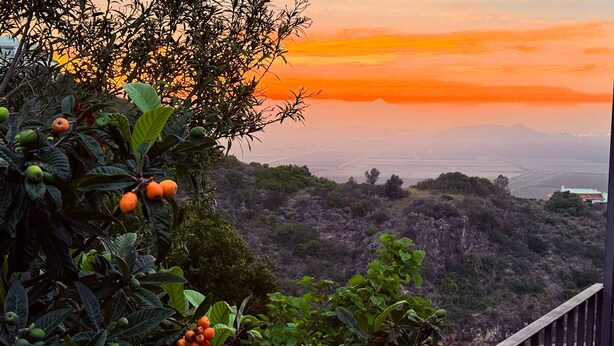 Ein Balkon mit Blick auf einen Sonnenuntergang über einer hügeligen Landschaft.