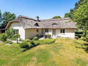 Ein Haus mit einem Strohdach, einer Ziegelaußenwand und einem gepflegten Rasen.