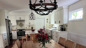 Una cocina amplia con armarios blancos, una mesa de comedor de madera, sillas de mimbre y un candelabro.