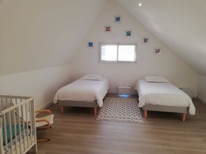 Ein Schlafzimmer mit zwei Betten, einem Babybett, einem Fenster und einem kleinen Nachttisch.
