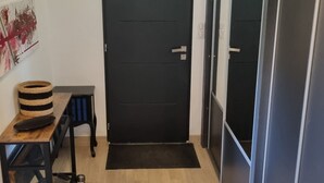 Ein Flur mit Holzboden, einer schwarzen Tür, einem kleinen Tisch mit einem Korb und einer Bank.