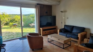 Ein Wohnzimmer mit Fernseher, Sofa, Couchtisch und einer Schiebetür, die in einen Garten führt.