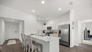 Una cocina moderna con armarios blancos, electrodomésticos de acero inoxidable y una isla central con taburetes de bar.