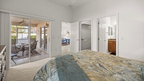 Un dormitorio con cama, ventilador de techo, puerta corrediza de vidrio que da a un patio y vestidor.