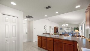 Una cocina amplia con una isla grande, armarios blancos y un comedor con candelabro.
