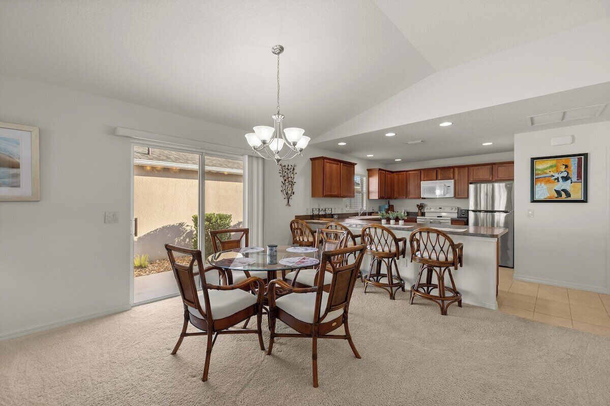 A modern kitchen with wooden cabinets, a dining area with wicker chairs, and a chandelier.