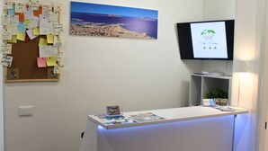 A reception desk with a 'Welcome' sign, a bulletin board with notes, a television screen, and a cityscape painting. - Room 8 A (Trapani)