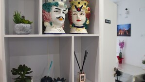 A shelf with decorative items including a plant, two figurines, and a reed diffuser. - Room 8 A (Trapani)