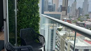 A balcony with two mesh chairs, a glass railing, and a cityscape view. - Modern Skyline Apartment in Marbella | Pool, Gym, and a Short Walk to the Cinta Costera (Panamá)