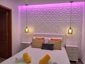 Ein Schlafzimmer mit einem gemusterten Kopfteil, zwei Nachttischlampen, einem Bett mit Kissen und einem Nachttisch.