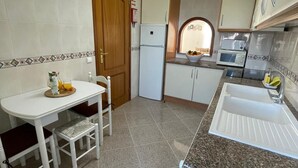 Una cucina compatta con frigorifero bianco, forno a microonde, lavandino e zona pranzo con tavolo e sedie.