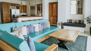 A modern living room with a teal sofa, wooden coffee table, and a kitchen area in the background. - Beachfront Luxury Villa in Playa Venao (Los Santos Province)