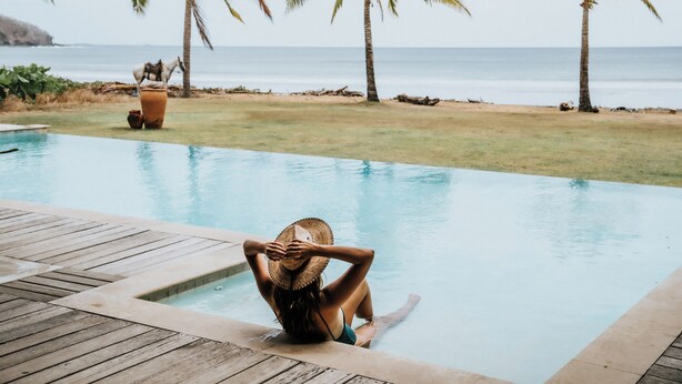 A person sitting by a pool with a view of the ocean and palm trees. - Beachfront Luxury Villa in Playa Venao (Los Santos Province)