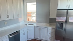 A kitchen with white cabinets, a stainless steel refrigerator, a ceiling fan, and a window. - Delightful and Remodeled 5-bedroom house near the North Shore and Draft Event (Pittsburgh)