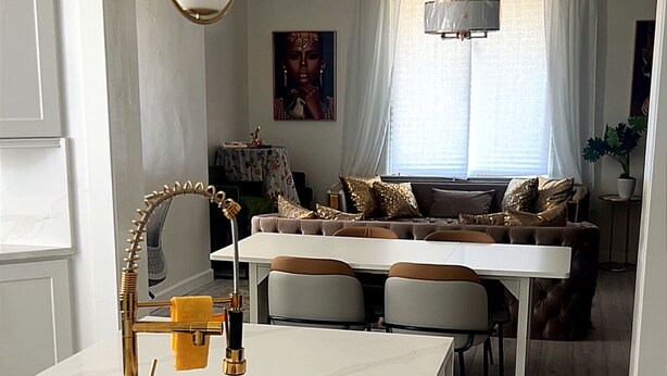 A modern kitchen with a marble countertop, gold faucet, and a dining area with a white table and chairs. - Delightful and Remodeled 5-bedroom house near the North Shore and Draft Event (Pittsburgh)