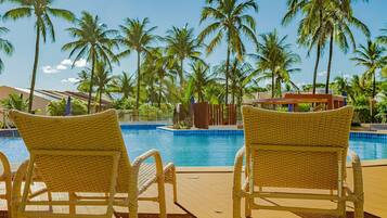 A poolside area with wicker chairs, a pool, and palm trees.