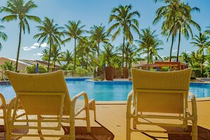 Ein Poolbereich mit Korbstühlen, einem Pool und Palmen.