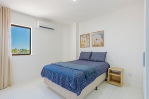 A bedroom with a bed, a nightstand, a window with curtains, and two wall-mounted pictures. - VT08 Great Apt for 3 people - Beachfront Cond. (Lauro de Freitas)