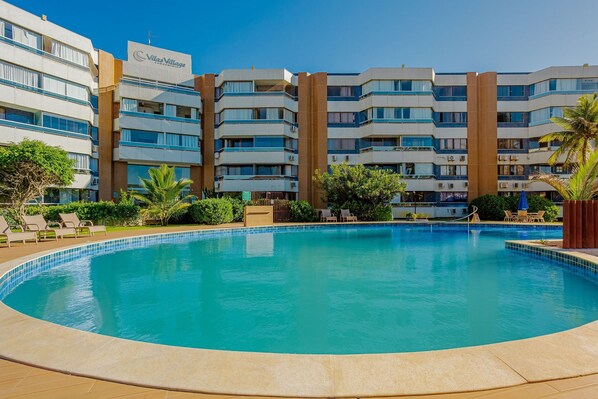 A hotel with a swimming pool, multiple balconies, and a sign reading 'Vilavillage.' - VT08 Great Apt for 3 people - Beachfront Cond. (Lauro de Freitas)