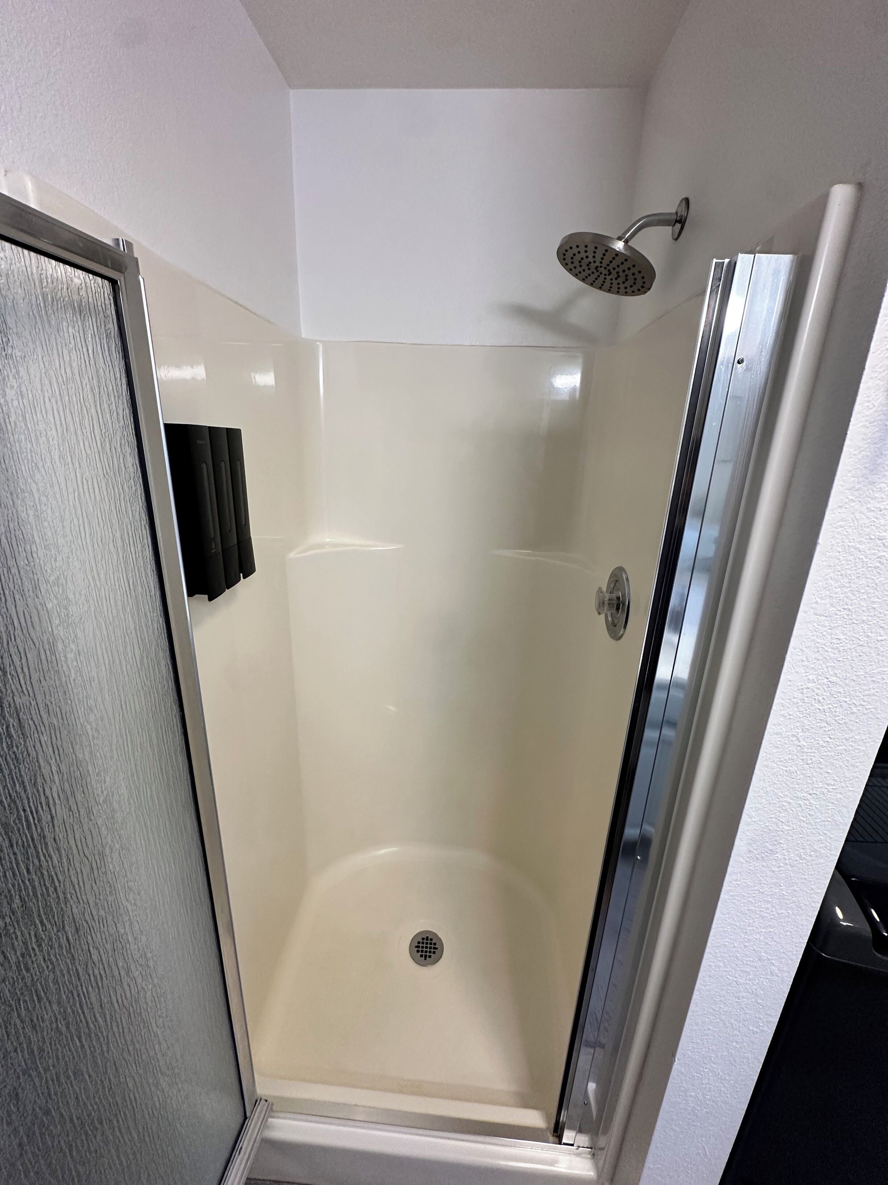 A glass-enclosed shower stall with a showerhead and a drain.