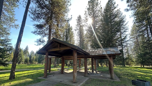 A wooden pavilion with benches, surrounded by a grassy area and tall trees. - Private Ptarmigan Suite (Hayden)