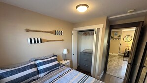 A bedroom with a bed, a bedside table with a lamp, a closet, and a door leading to another room. - Private Ptarmigan Suite (Hayden)