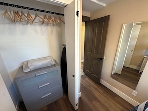 A room with a grey dresser, a wooden coat rack, a door, and a mirror reflecting the room.