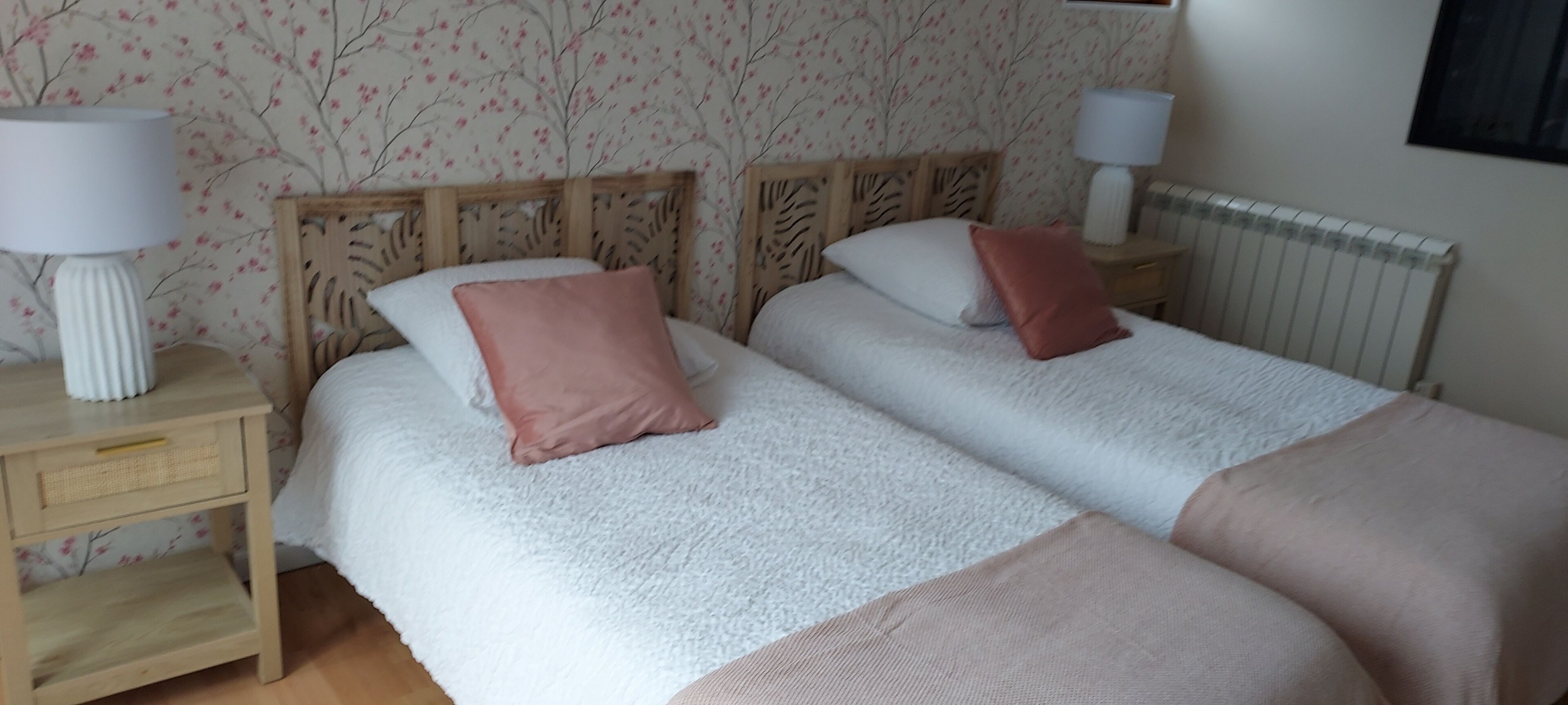 Una cama doble con cabecera de madera, dos mesitas de noche con lámparas y un radiador.