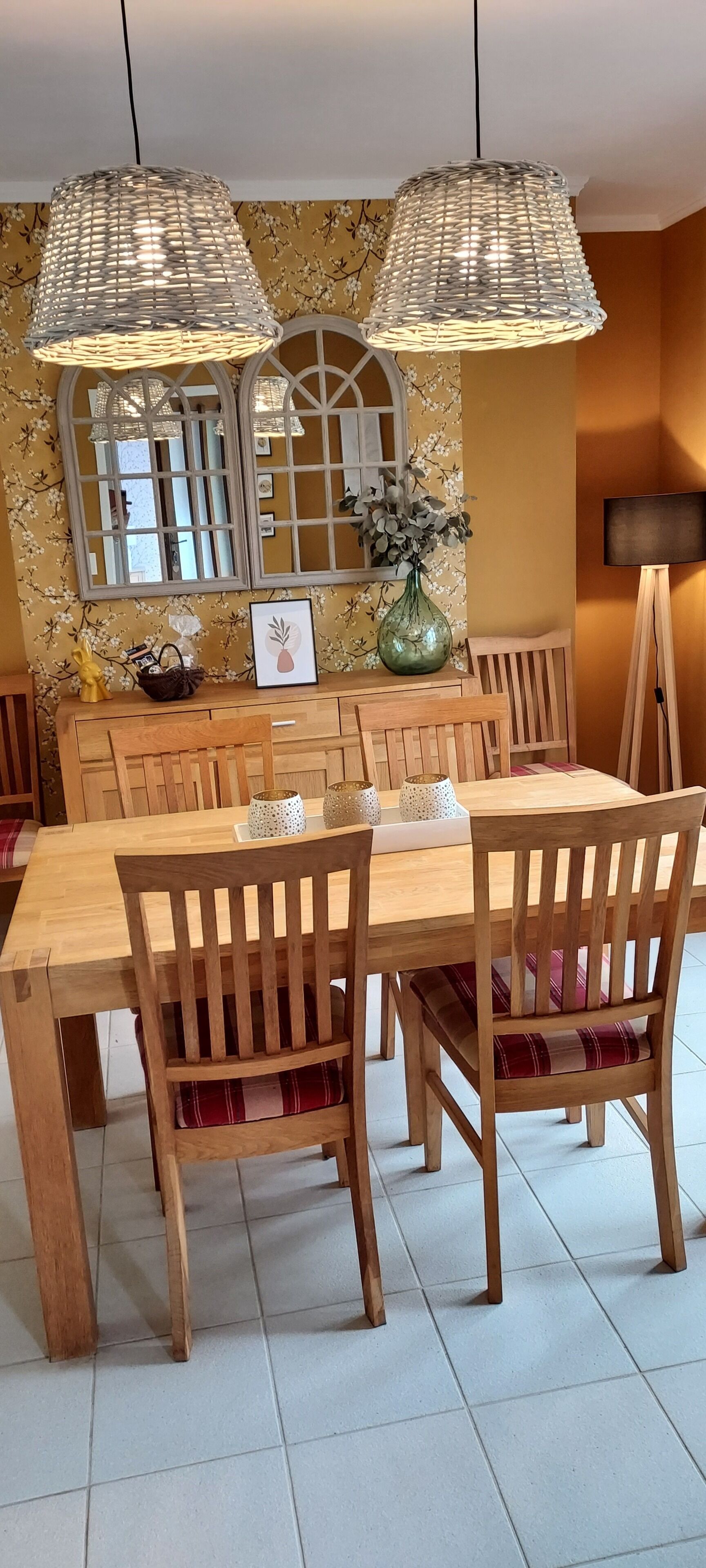 Een eethoek met een houten tafel en stoelen, een vaas met bloemen en een spiegel aan de muur.
