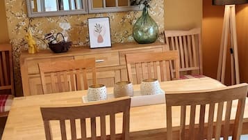 Een eethoek met een houten tafel en stoelen, een vaas met bloemen en een spiegel aan de muur.
