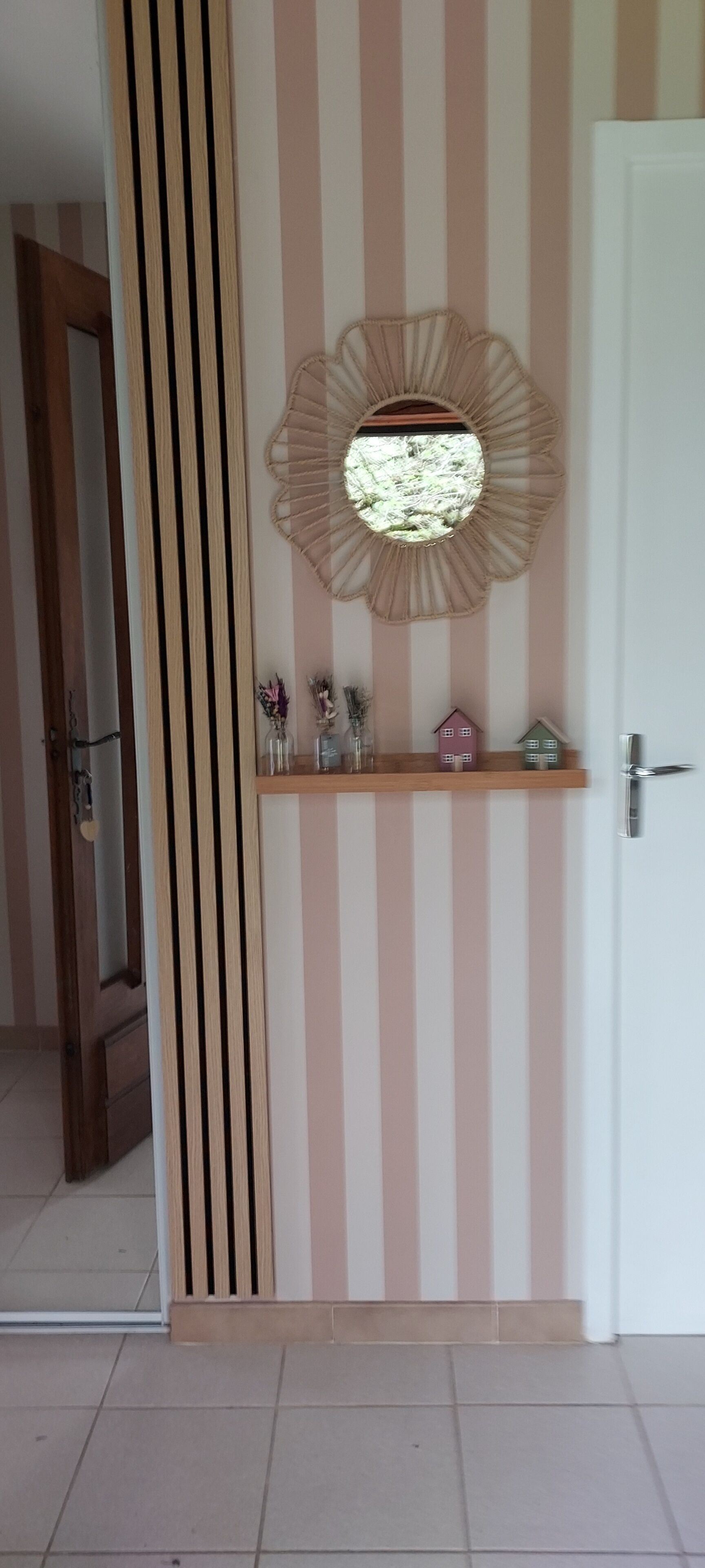 Een kamer met een gestreepte wand, een ronde spiegel, een plankje met kleine objecten en een deur.