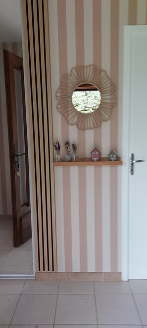 A room with a striped wall, a round mirror, a shelf with small items, and a door. - Le Mûrier single-storey house with beautiful veranda. Beautiful garden. (Gramat)